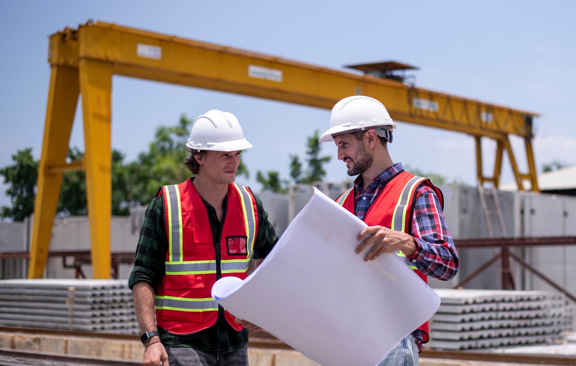 Engineer or worker in safety gear at a construction site, wearing a hard hat and reflective vest, examining blueprints.