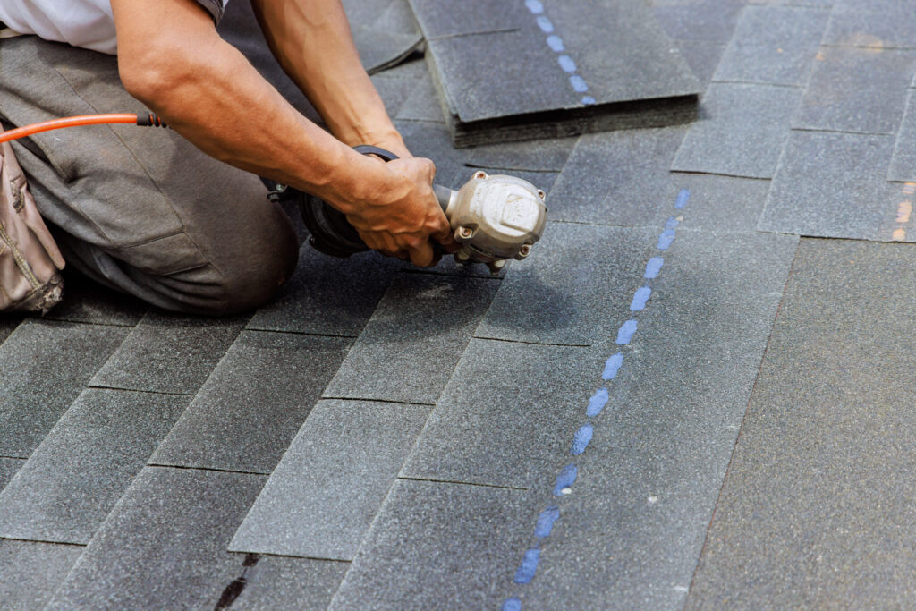 Roofer installing new asphalt bitumen shingles with pneumatic air nail gun, showcasing roofing services Jacksonville FL.