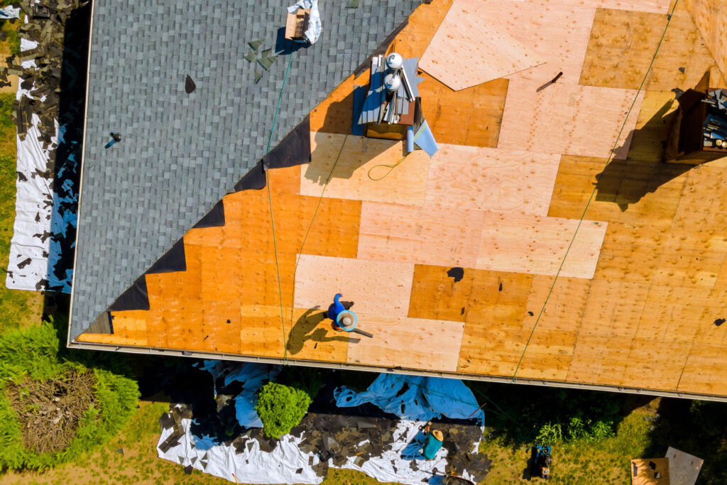Worker replacing old asphalt shingles on a roof, showcasing roofing services Jacksonville FL.