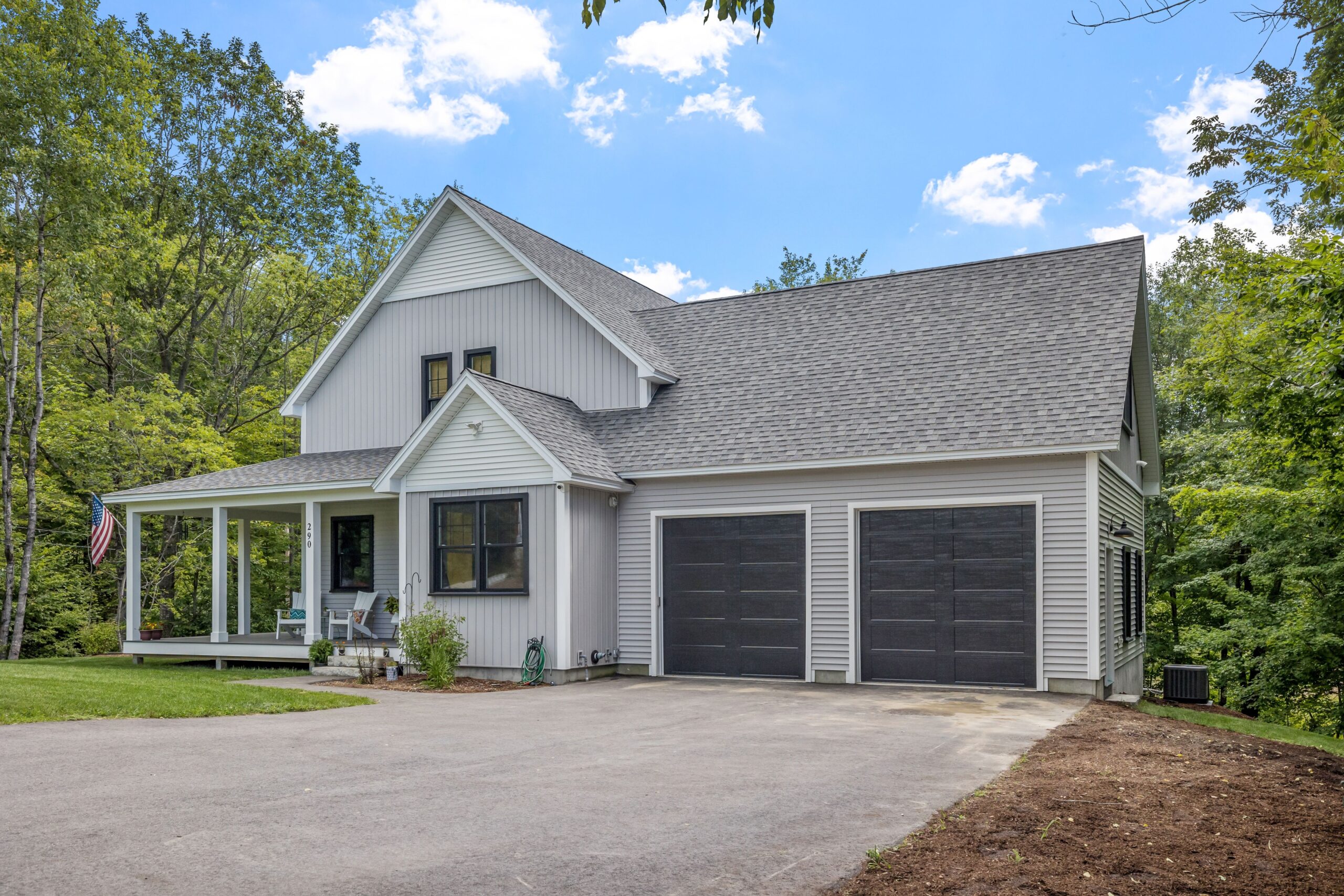 Modern New England Colonial home with American flag, featuring a white facade, black shutters, and a manicured lawn.