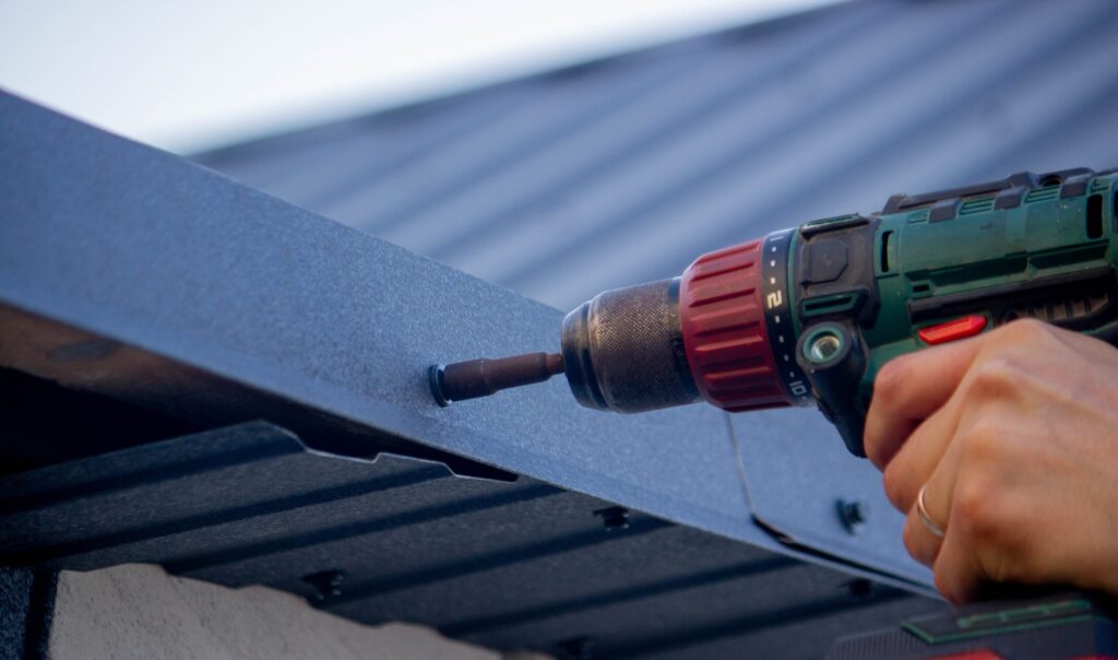 A man on a roof in Jacksonville, FL, tightens a self-tapping screw, showcasing roofing services Jacksonville FL.