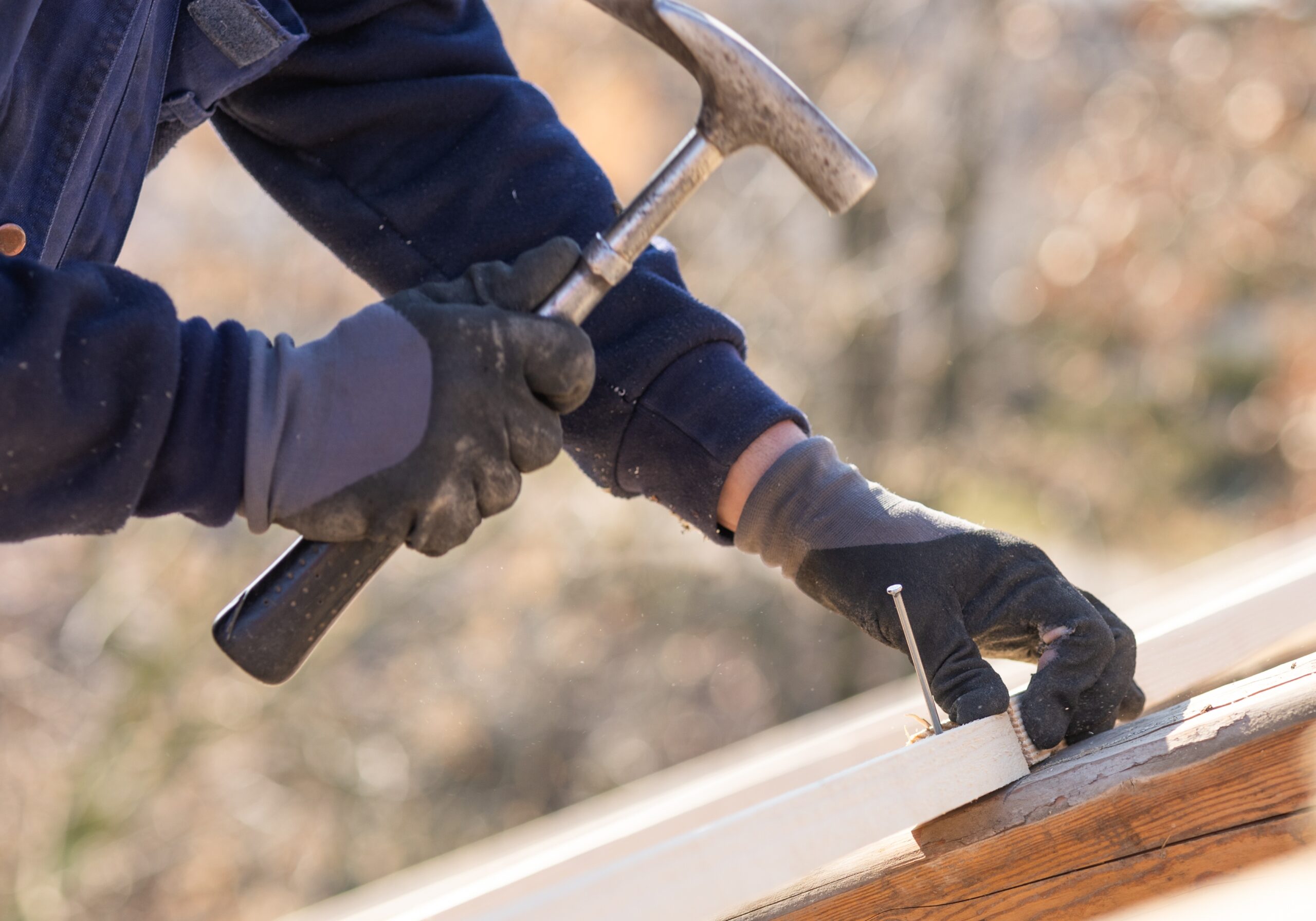 Construction worker nailing wood board with hammer, showcasing craftsmanship by Polaris Roofing Solutions Jacksonville FL.