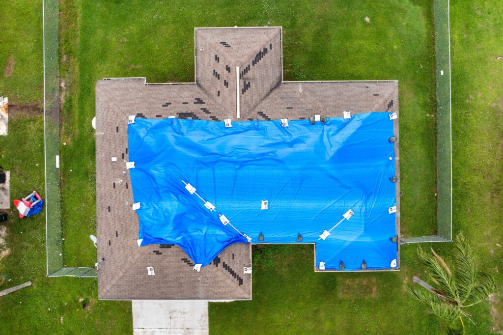 Rooftop wrapped in a blue plastic tarp for protection after hurricane damage, highlighting roofing services Jacksonville FL.
